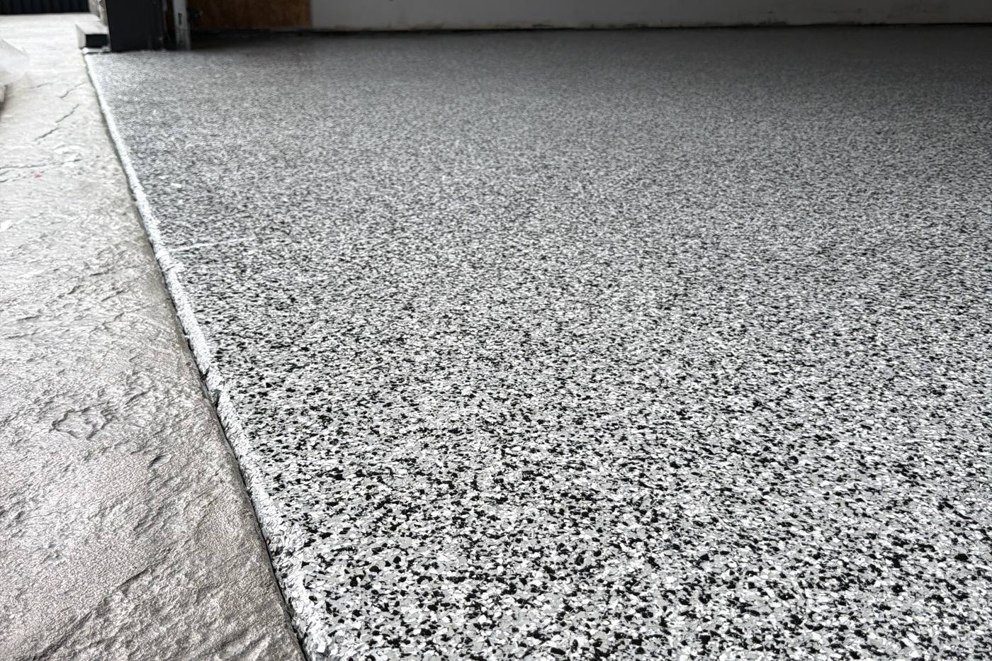 Close detail of black and white decorative flake garage floor coating at the threshold